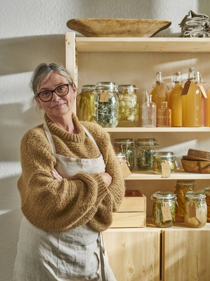 Žena stojí před policovou sestavu IVAR se sklenicemi a lahvemi KORKEN v policích.