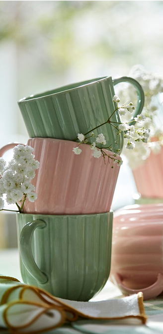 Světle zelené a růžové hrnky SMÖRFISK mezi jemnými bílými květy navozují svěží a živou atmosféru.