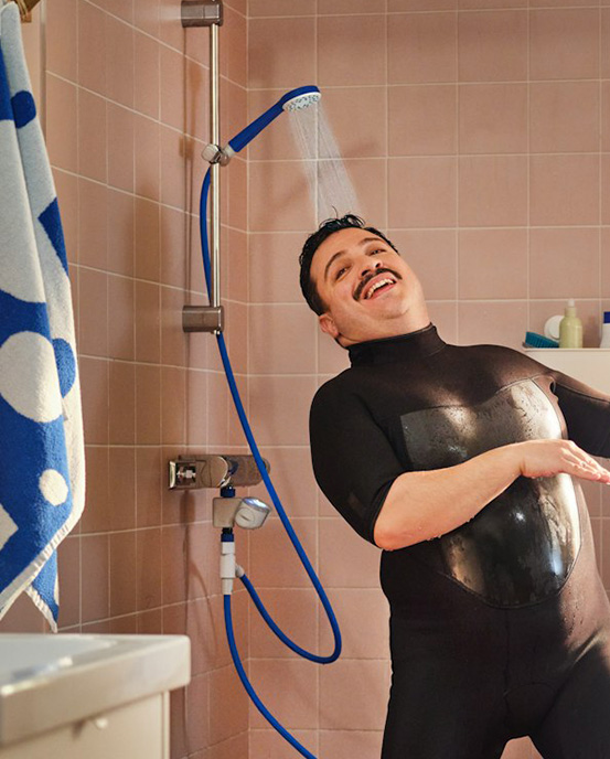 Muž se sprchuje v neoprenu pod sprchou BERGVATTNET.