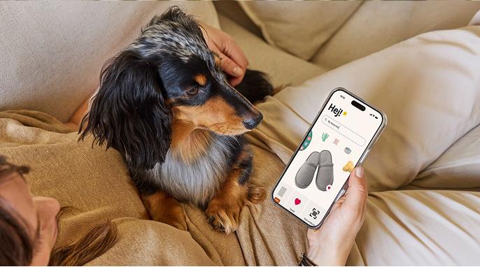 Osoba si prohlíží v mobilu aplikaci IKEA, na klíně jí sedí pes.