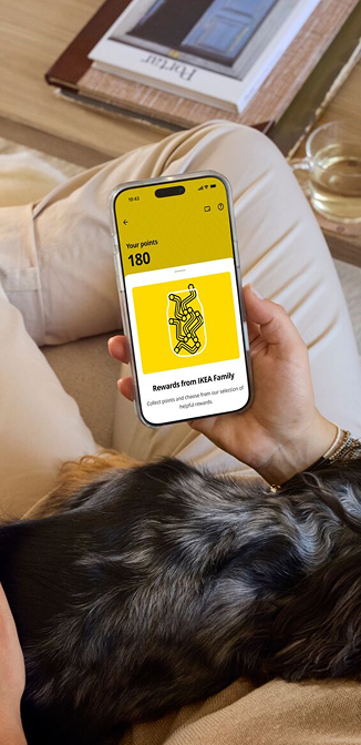 Osoba leží na gauči, na klíně má psa a v ruce drží mobil s aplikací IKEA.