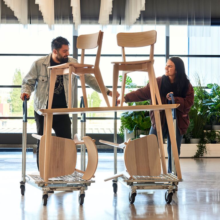 Dvě osoby vezou na nákupních vozících jídelní stůl a 4 židle. 